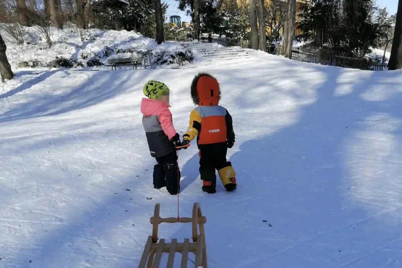 Zwei Kinder spielen im Winter mit einem Schlitten im Bienertpark Dresden – Kindertagespflege Am Bienertpark